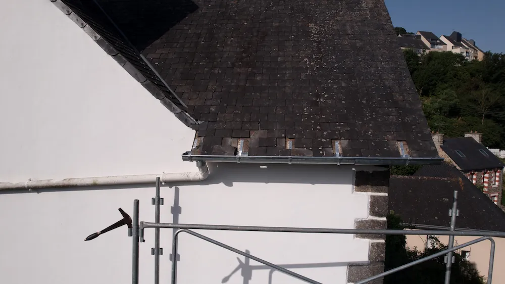 Artisan couvreur-zingueur de l'entreprise Armor Couverture 22 en plein travail de fixation d'une gouttière neuve sur le toit d'une maison à Saint-Brieuc.